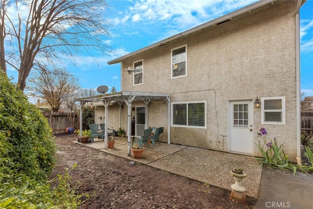 rear view of house featuring stucco siding, a patio area, fence, and a pergola