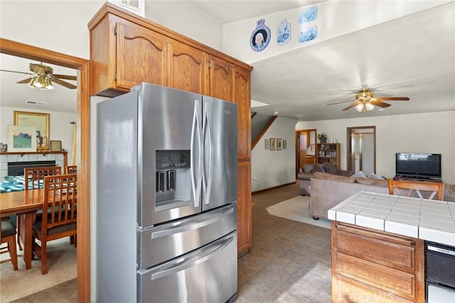 kitchen featuring tile countertops, a ceiling fan, open floor plan, brown cabinets, and stainless steel fridge