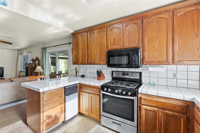 kitchen featuring black microwave, a peninsula, open floor plan, backsplash, and gas range