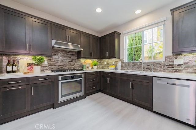 kitchen featuring stainless steel appliances, light countertops, a sink, dark brown cabinets, and under cabinet range hood