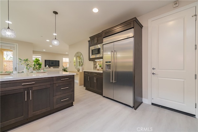 kitchen with pendant lighting, light countertops, light wood-style flooring, dark brown cabinets, and built in appliances