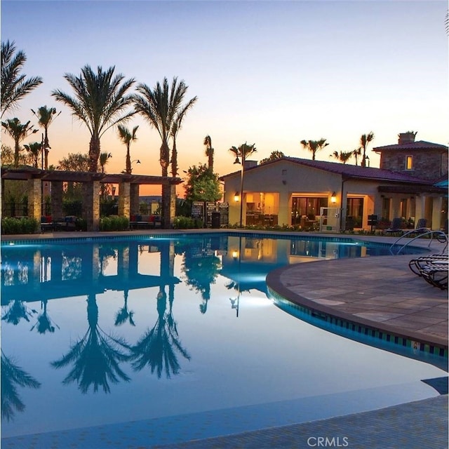 pool at dusk with a patio and a community pool