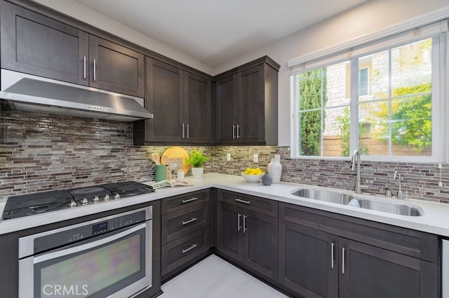 kitchen with dark brown cabinetry, appliances with stainless steel finishes, light countertops, under cabinet range hood, and a sink