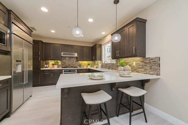 kitchen with dark brown cabinetry, appliances with stainless steel finishes, a peninsula, light countertops, and under cabinet range hood