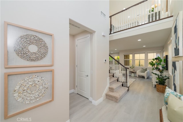 foyer with baseboards, visible vents, a towering ceiling, stairway, and wood finished floors