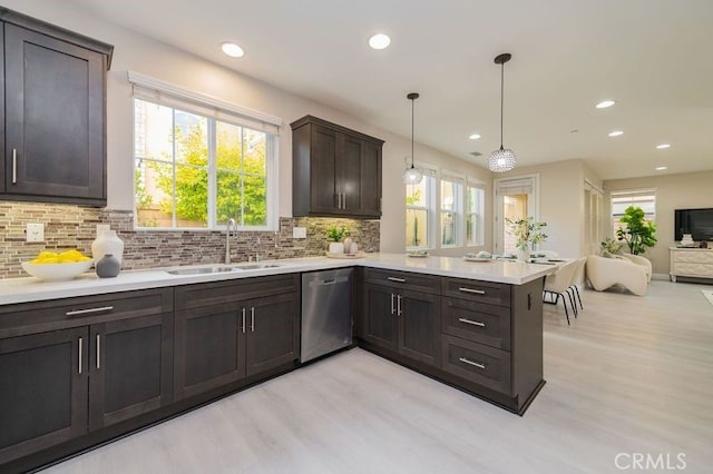 kitchen with light countertops, backsplash, a sink, dishwasher, and a peninsula