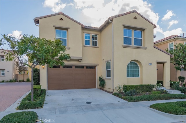 mediterranean / spanish home with a tiled roof, decorative driveway, an attached garage, and stucco siding