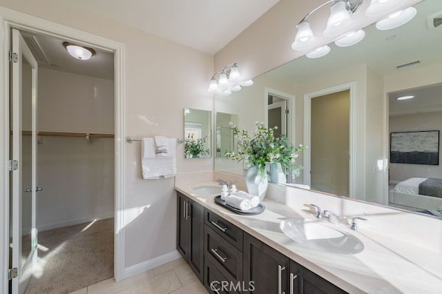 ensuite bathroom featuring double vanity, visible vents, connected bathroom, a spacious closet, and a sink