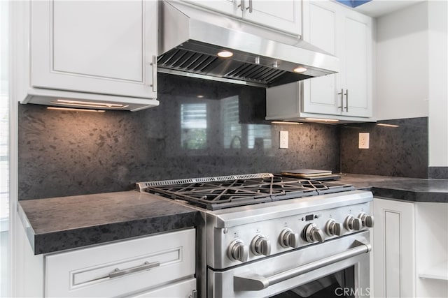 kitchen featuring dark countertops, high end stainless steel range oven, decorative backsplash, white cabinetry, and under cabinet range hood