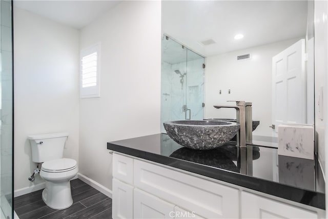 bathroom featuring toilet, wood finish floors, visible vents, vanity, and a marble finish shower