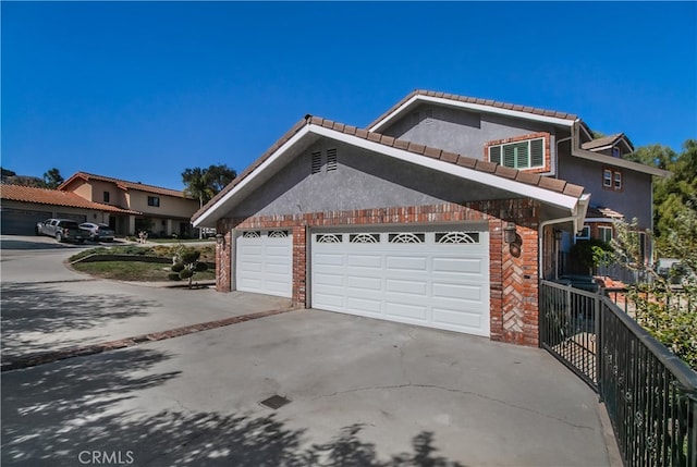 view of property exterior featuring an attached garage, brick siding, fence, driveway, and stucco siding