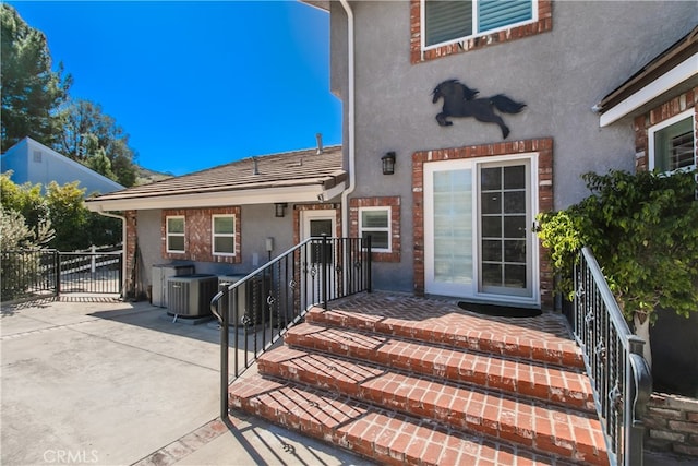 entrance to property with central air condition unit, fence, and stucco siding