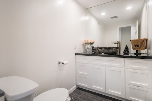 half bath featuring visible vents, toilet, wood tiled floor, vanity, and baseboards