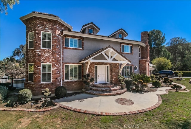 view of front of property featuring brick siding, fence, a front lawn, and stucco siding