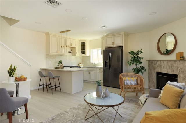 living area featuring light wood-style floors, visible vents, a high end fireplace, and baseboards