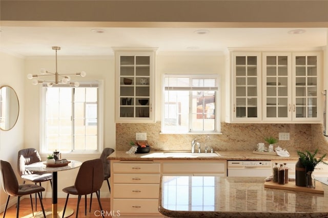 kitchen with light stone countertops, ornamental molding, a sink, dishwasher, and backsplash