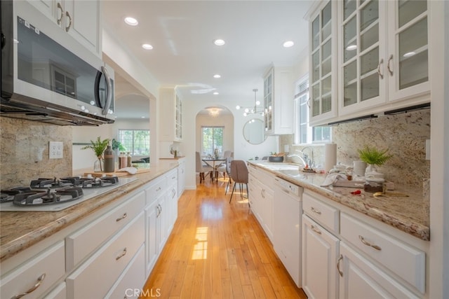 kitchen with light wood-type flooring, a sink, white cabinetry, white appliances, and arched walkways