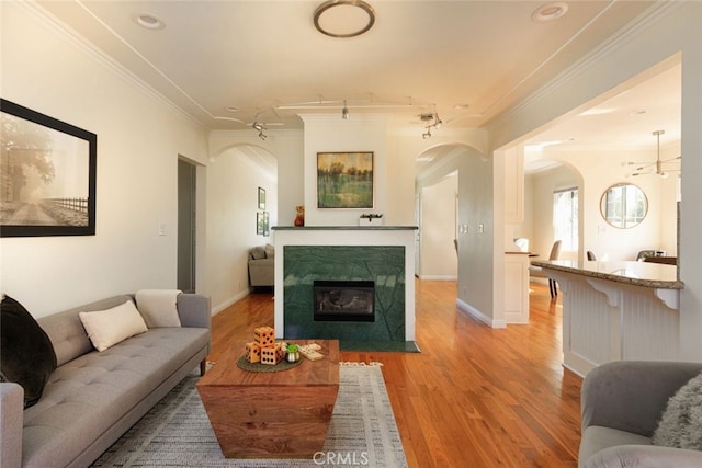 living area featuring arched walkways, a fireplace with flush hearth, light wood-style flooring, and ornamental molding