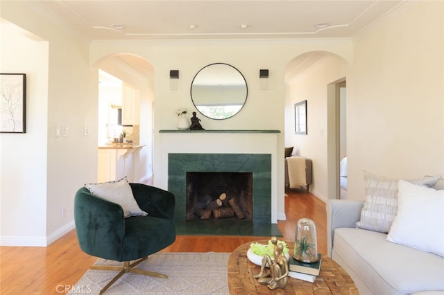 living room with crown molding, light wood-style floors, and a high end fireplace