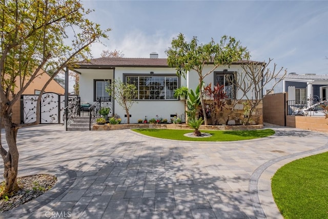 view of front of home featuring decorative driveway, a gate, fence, and stucco siding