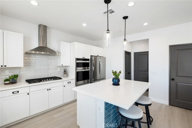 kitchen featuring visible vents, decorative backsplash, wall chimney exhaust hood, a center island, and stainless steel appliances