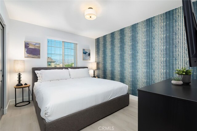 bedroom with an accent wall, baseboards, and light wood finished floors