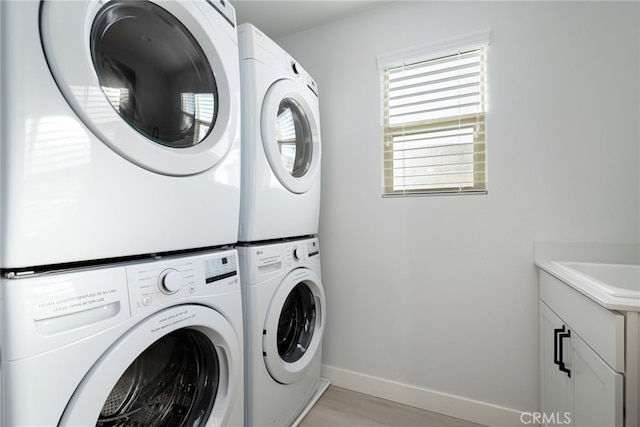 washroom featuring cabinet space, baseboards, light wood-style flooring, stacked washing maching and dryer, and a sink