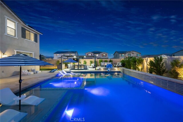 pool at night with a patio area, a pool with connected hot tub, and fence