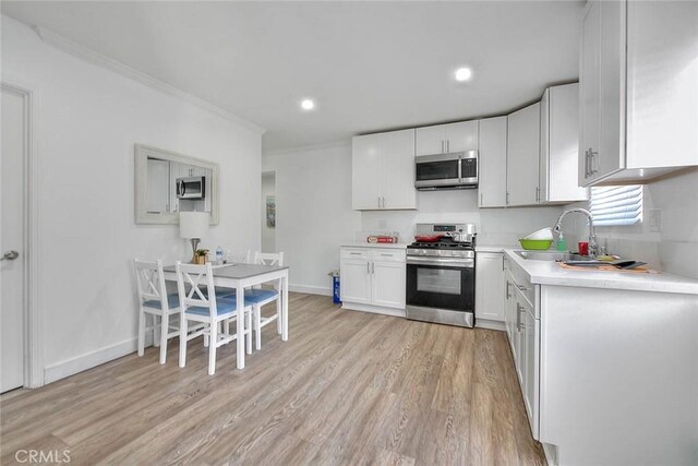 kitchen with white cabinets, light wood-style flooring, stainless steel appliances, light countertops, and a sink