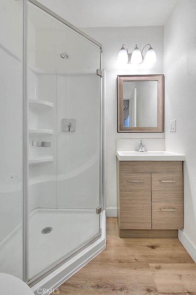 full bath featuring a stall shower, wood finished floors, vanity, and baseboards