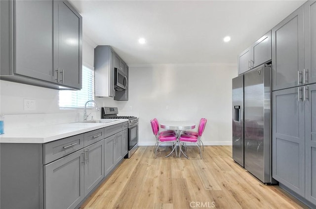 kitchen featuring gray cabinetry, stainless steel appliances, a sink, baseboards, and light countertops