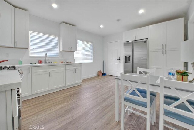 kitchen featuring a sink, white cabinets, light countertops, stainless steel fridge with ice dispenser, and light wood finished floors