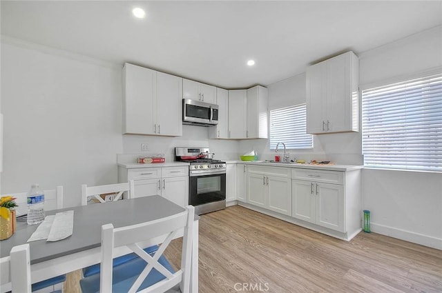 kitchen featuring a sink, white cabinetry, light countertops, appliances with stainless steel finishes, and light wood finished floors