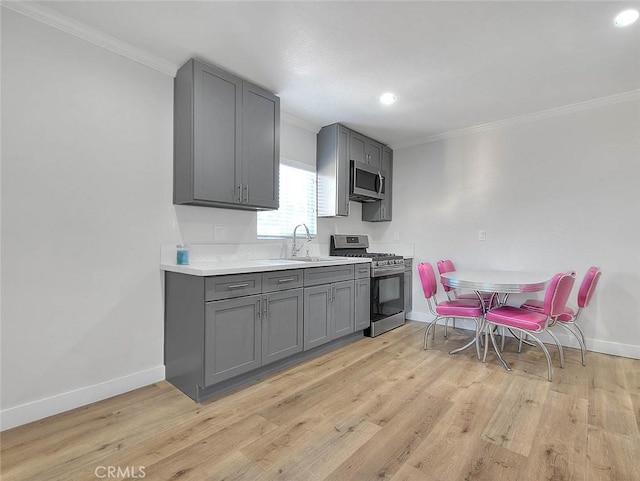 kitchen featuring light wood-style floors, appliances with stainless steel finishes, a sink, and gray cabinetry