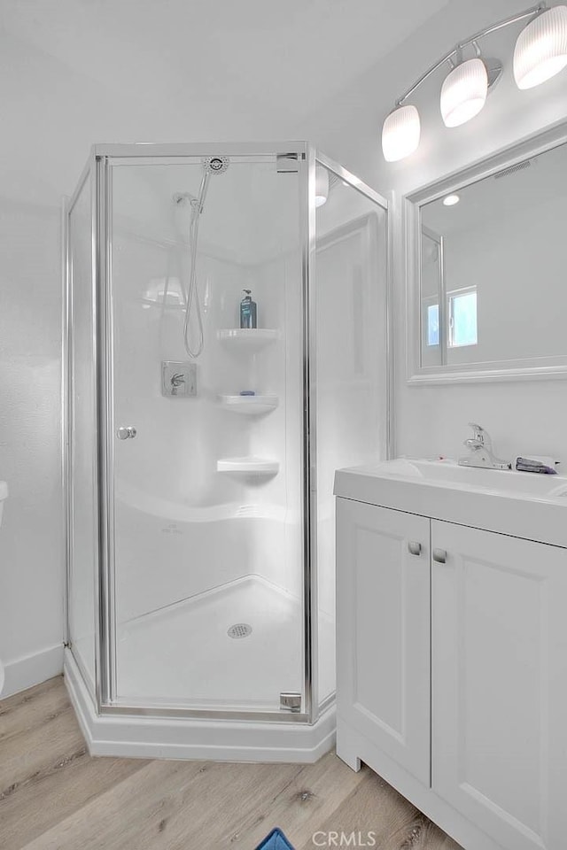 bathroom with wood finished floors, a shower stall, and vanity