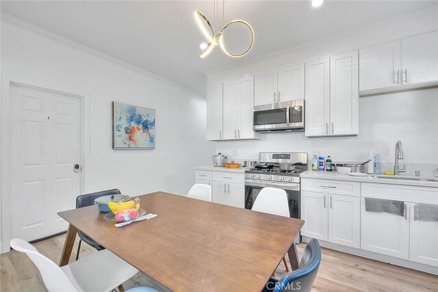 kitchen with appliances with stainless steel finishes, white cabinets, a sink, and light wood finished floors