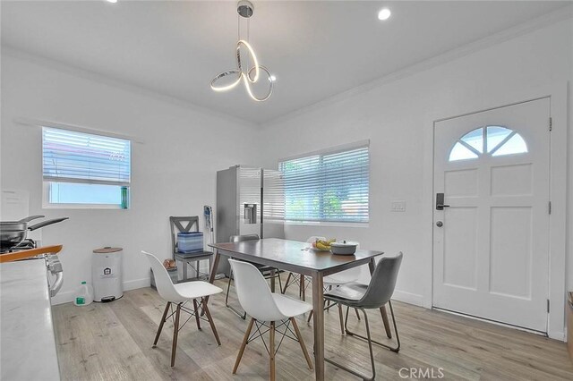 dining area with crown molding, light wood-style flooring, baseboards, and an inviting chandelier