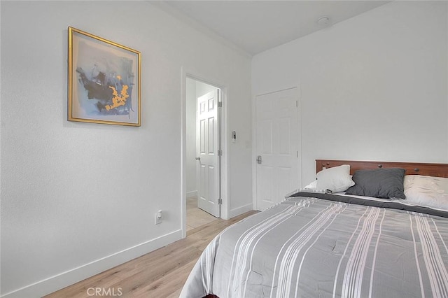 bedroom with ensuite bathroom, light wood-type flooring, and baseboards