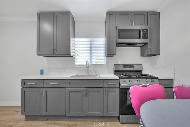 kitchen with stainless steel appliances, crown molding, a sink, and gray cabinetry