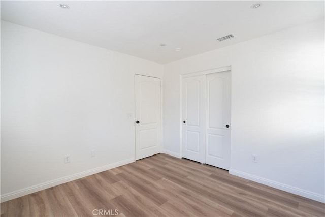 unfurnished bedroom with a closet, visible vents, baseboards, and wood finished floors