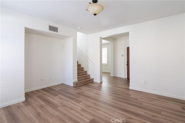 empty room featuring light wood-type flooring, visible vents, stairway, and baseboards