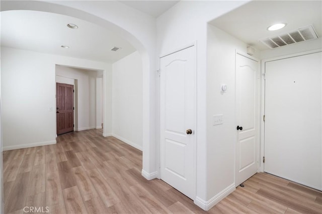 corridor featuring arched walkways, light wood finished floors, visible vents, and baseboards