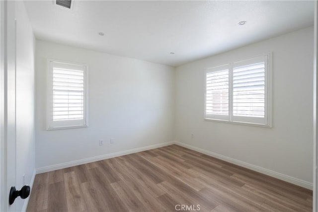 spare room featuring baseboards, wood finished floors, and a healthy amount of sunlight