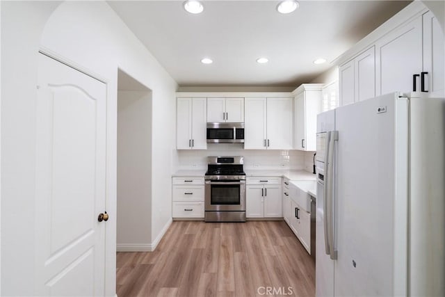 kitchen featuring light wood-style flooring, appliances with stainless steel finishes, light countertops, white cabinetry, and backsplash