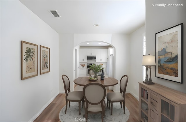 dining area featuring baseboards, visible vents, arched walkways, and wood finished floors