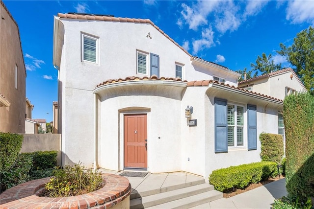 view of front facade featuring fence, a tiled roof, and stucco siding