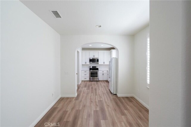 hallway featuring light wood-type flooring, baseboards, visible vents, and arched walkways