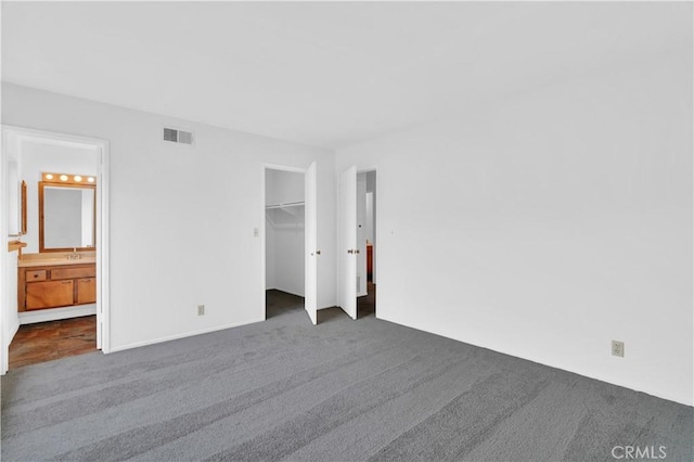 unfurnished bedroom featuring visible vents, ensuite bathroom, a spacious closet, dark colored carpet, and a closet