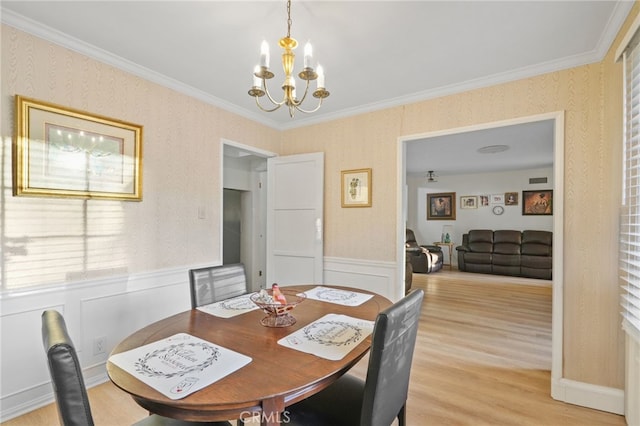 dining space with light wood-type flooring, ornamental molding, wainscoting, wallpapered walls, and a chandelier