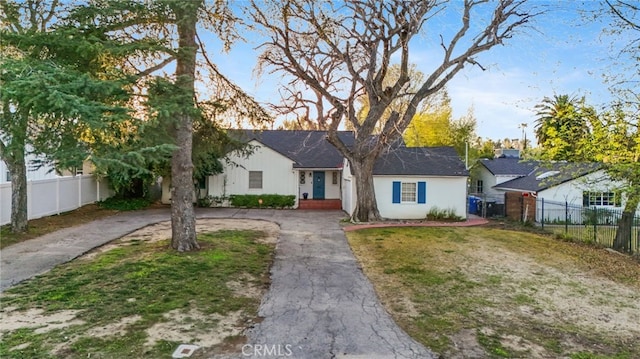 view of front facade featuring stucco siding, a front lawn, driveway, and fence